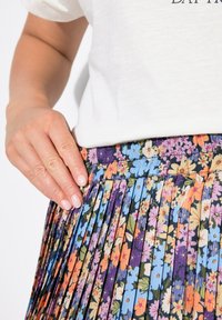 Blumigen Faltenrock mit dunklem Hintergrund und bunten Blumen in Blau, Orange und Lila; strukturierter Stoff mit sichtbarem Bündchen.