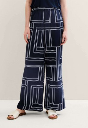 Navy wide-leg pants with white geometric pattern, elastic waistband, and lightweight fabric. Paired with light-colored flat sandals.