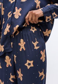 Marineblauw pyjama set met afbeeldingen van peperkoekmannetjes en vakantie-thema patronen. Zachte stof met een elastische taille en een overhemd met knopen.