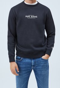 Námořnická modrá bavlněná mikina s žebrovaným kulatým výstřihem a manžetami, na přední straně má bílé logo "PEPE JEANS" a diamantové logo na rukávu.