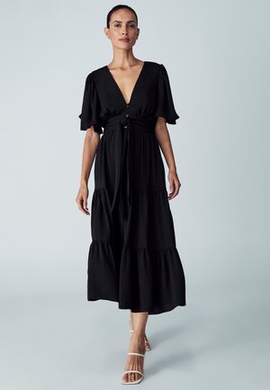 Black, tiered maxi dress with a deep V-neck, short puff sleeves, cinched waist, and a tie detail. Smooth texture, casual design.