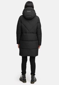 Sort pufferjakke med hætte, prydet med et chevron-quiltet design. Jakken går til midt på låret og har sidelommer.