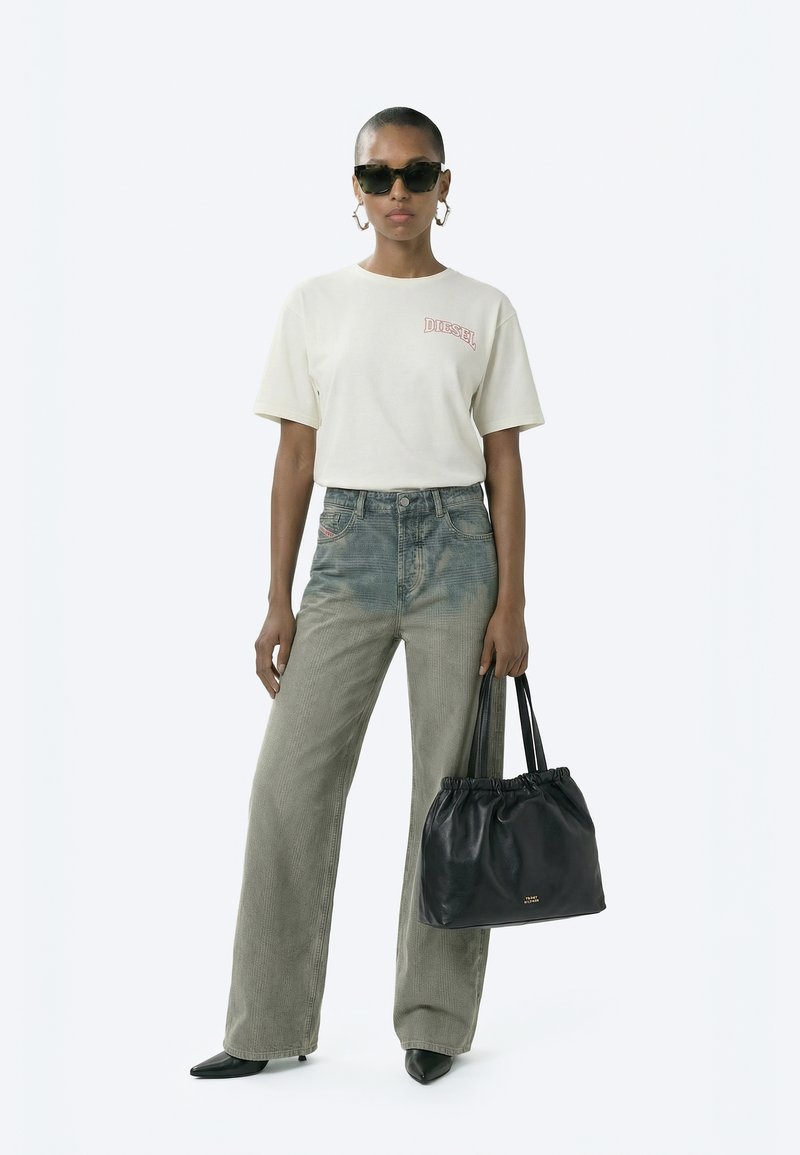 Femeie purtând un tricou alb Diesel, blugi largi cu talie înaltă, de culoare gri estompat, pantofi negri cu vârf ascuțit, ochelari de soare cu rame în formă de ochi de pisică, ținând o geantă tote neagră din piele plisată.