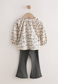 Long-sleeve blouse in cream with black bow and flower print; paired with dark gray ribbed bell-bottom pants. Textured fabric; elastic cuffs.