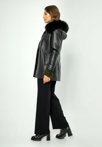 Zwarte leren jas met een bontcapuchon, zijzakken en groene manchetaccenten, gecombineerd met zwarte wijde pantalon en chunky haklaarzen.