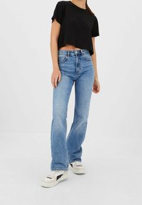 Jeans di denim azzurro chiaro a zampa d'elefante con vita alta, caratterizzati da un design a cinque tasche, lievi effetti di usura e una t-shirt nera corta.