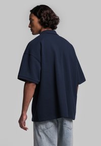 Przestronna granatowa koszulka polo z miękkiej bawełny, z klasycznym kołnierzykiem i krótkimi rękawami. Tył ma prosty, bezszwowy design.