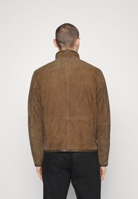 Brun mockakjol med hög krage, strukturerade sömmar och slät textur. Har en rak passform och minimalistisk detaljering.