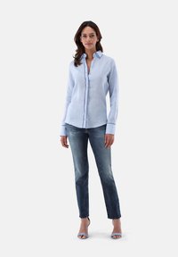 Light blue linen button-up shirt with long sleeves, paired with dark denim jeans, and light blue strappy heels.