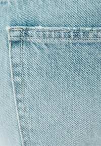 Light blue denim fabric featuring a textured surface with a pocket detail and visible stitching, showcasing a classic jean design.