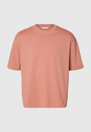 Egyszerű, rövid ujjú, kerek nyakú póló tompa terrakotta színben, laza szabással, világosszürke háttéren.