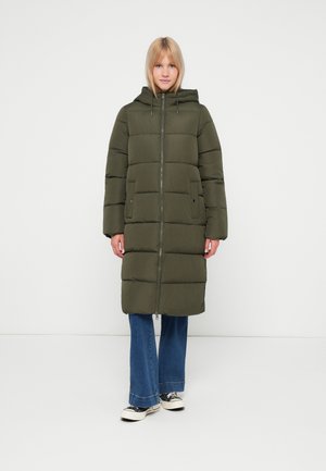 Padded green parka coat with a zip front, hood, and side pockets, featuring a boxy silhouette and textured fabric. Paired with flared jeans.