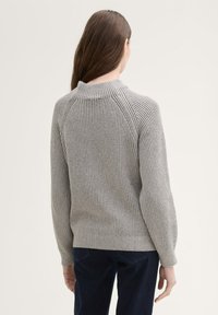 Grijze geribbelde gebreide trui met een hoge kraag en raglanmouwen, voorzien van een aansluitende taille en lange mouwen.