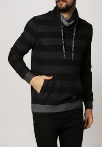 Czarna i szara bluza z kapturem w paski, z kołnierzem typu komin, przednią kieszenią i sznurkiem do ściągania. Wykonana z miękkiego materiału z prążkowanymi mankietami i dołem.