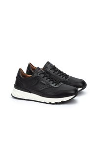 Zapatillas de cuero negro con un diseño texturizado, suela blanca acolchada y cierre con cordones. Presenta perforaciones sutiles y acentos de marca.