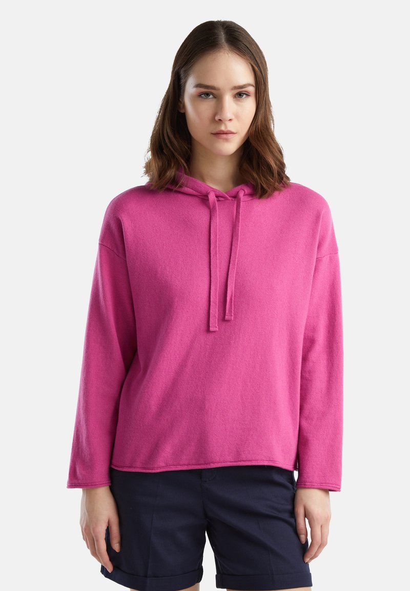 Różowa bluza z kapturem, długie rękawy, okrągły dekolt, sznurek i miękka tekstura. W połączeniu z granatowymi szortami.
