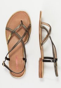 Sandales en cuir marron avec des brides croisées métalliques noires, accent en or autour de la semelle, semelle plate et une petite boucle sur la sangle de la cheville.