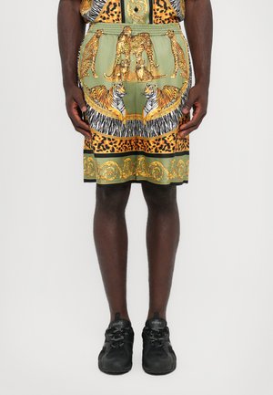 Grüne Shorts mit Muster, die Leoparden und Tiger zeigen, kombiniert mit verschiedenen Tiermotiven und goldenen Akzenten, abgeschlossen mit einem elastischen Bund.