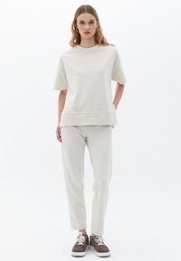 Licht beige sweatshirt en bijpassende taps toelopende broek van een zachte stof. De outfit heeft een relaxed fit met korte mouwen en zijzakken.