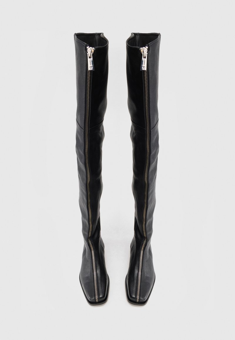 Svarta läderstövlar över knäna med en strömlinjeformad design, som har två sidodragkedjor, fyrkantiga tår och en jämn yta.