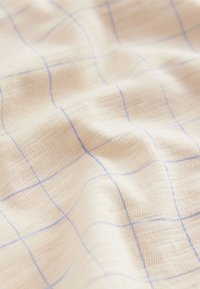 Lysebeige stof med en tekstureret overflade, der har et subtilt blåt ternet mønster. Blødt, vævet materiale med en glat finish.