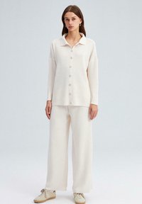 Conjunto de punto acanalado en beige claro que incluye una blusa de cuello con botones y pantalones de pierna ancha, con una textura suave y una silueta relajada.
