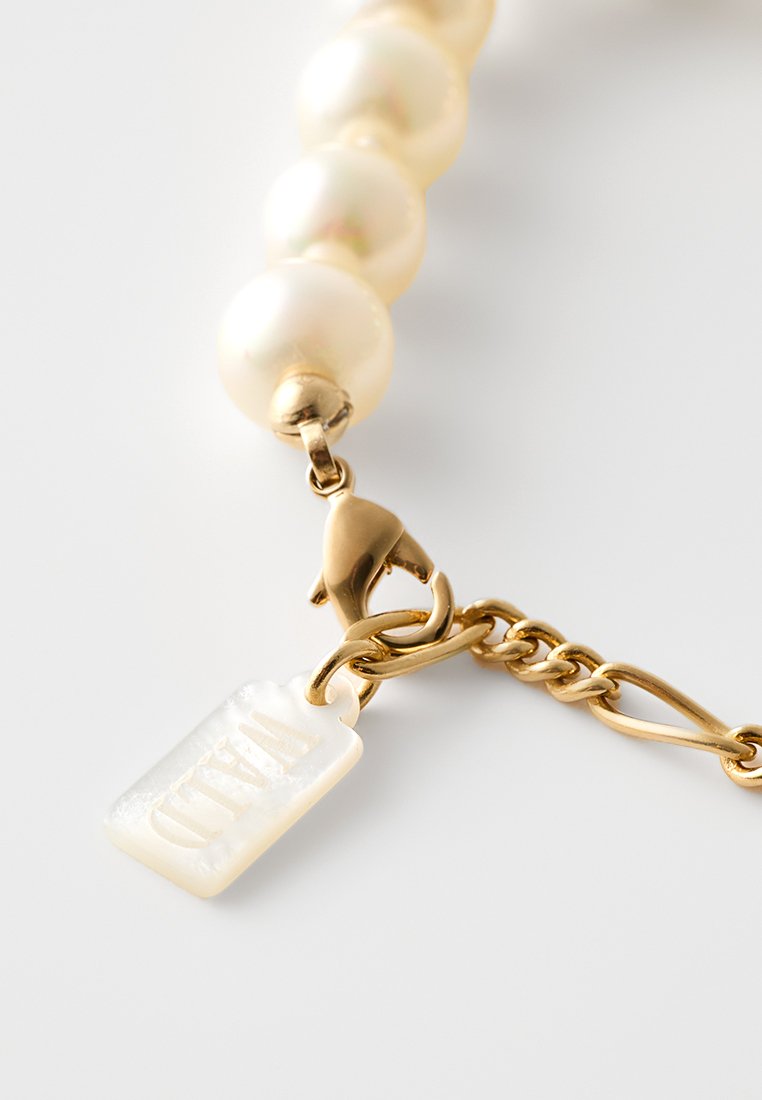 Parelarmband met gouden hardware, gekenmerkt door een kreeftsluiting en een rechthoekig label met de opstaande tekst "WILD".