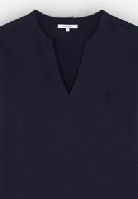 Donker marineblauw shirt met een klein "SCP" logo geborduurd op de borst en een V-hals met inkeping, maat small label zichtbaar aan de binnenkant.