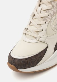 Sneaker con tomaia sintetica color crema, sovrapposizione in tessuto marrone testurizzato, lacci neutri e suola in gomma per una maggiore aderenza.