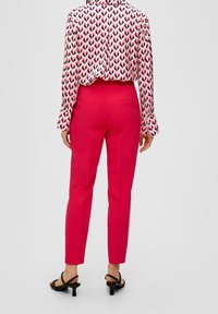 Pantaloni aderenti rosa con una texture liscia, dotati di una tasca posteriore. Abbinati a una blusa a maniche lunghe con motivo e sandali neri con tacco.