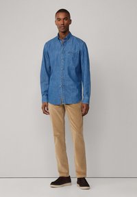 Lichtblauw denim overhemd met knopen en een borstzak, gecombineerd met beige corduroy broek en donkerbruine schoenen. Zachte textuur.