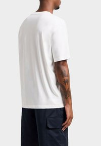 T-shirt bianco a maniche corte con collo rotondo. Tessuto morbido con orlo dritto e vestibilità comoda. Abbinato a pantaloni cargo blu navy.