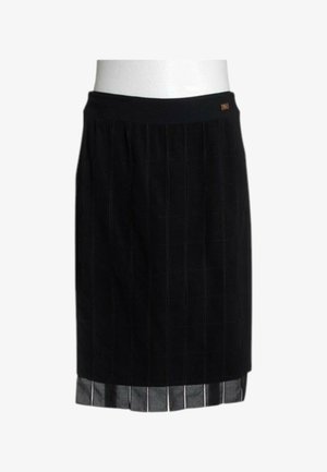 Jupe noire longueur genou avec coutures verticales, taille ajustée et doublure à rayures argentées qui dépasse de l'ourlet.