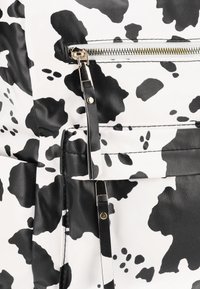 Zaino con stampa a macchie di mucca in bianco e nero, con texture in ecopelle, cerniera dorata e dettagli neri su spallacci e attacchi.