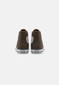 Sneaker alte marroni in pelle con suole in gomma bianca. Presentano una toppa circolare con logo e scritte nere sul tallone.