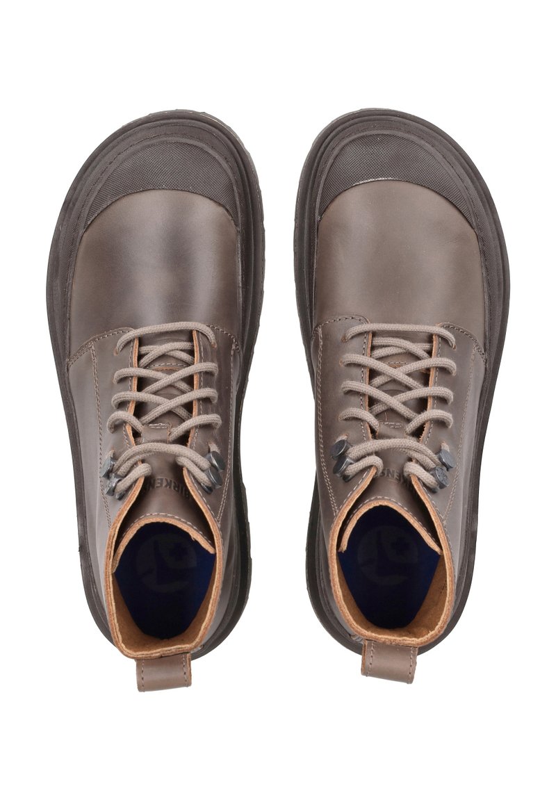 Stivali in pelle marrone con punta arrotondata, sole in gomma e accenti beige a contrasto. Presentano lacci grigi e una caviglia imbottita per supporto.