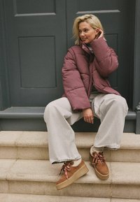 Red quilted puffer jacket, grey wide-leg trousers, and brown platform shoes with patterned laces, seated on stone steps.