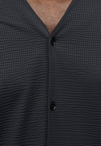 Σκούρο γκρι πουκάμισο με κοντά μανίκια και κουμπιά, κατασκευασμένο από υφασμάτινη ύφανση-γουάφλ με υφή. Διαθέτει V-λαιμόκοψη και δύο μαύρα κουμπιά στο εμπρόσθιο μέρος.