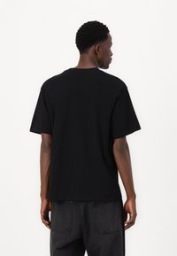 T-shirt nero a maniche corte con scollo rotondo, vestibilità comoda e realizzato in morbido cotone, visto da dietro, con cuciture sottili.