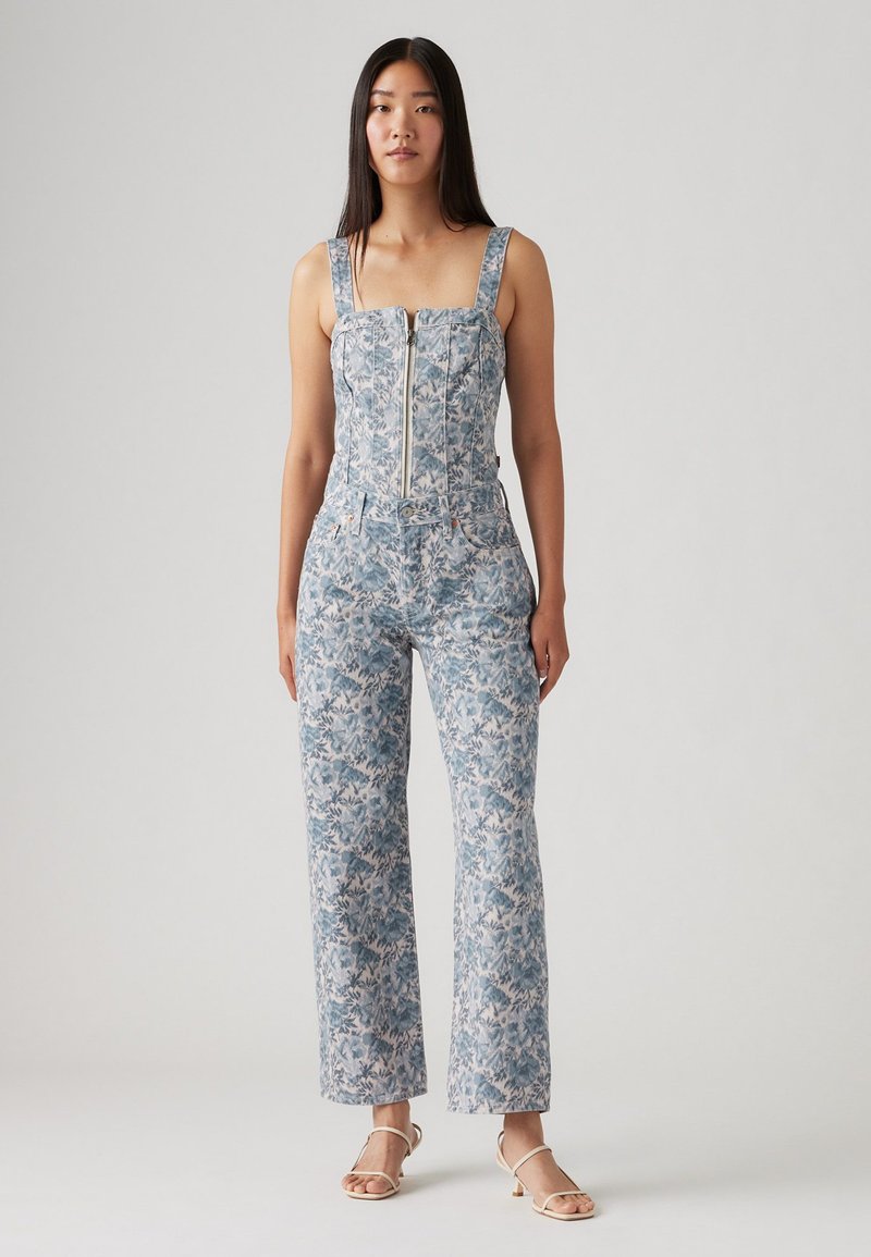 Combinaison florale bleu clair, avec un buste ajusté et fermeture éclair, des bretelles larges et un pantalon évasé avec des motifs décoratifs.