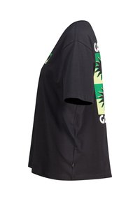 Mustan puuvillan t-paita, jossa on vihreä ja keltainen graafinen suunnittelu, jossa on palmulehtiä ja tekstiä. Lyhyet hihat, rento istuvuus ja sivulogo.