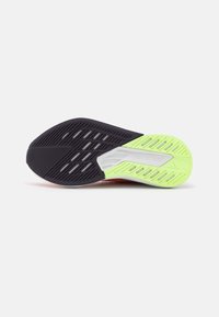 Semelle de chaussure présentant un design multi-texturé, principalement en noir avec des accents vert vif, des zones aérées et le logo "LIGHTSTRIKE".