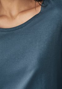 Blauwe katoenen t-shirt met een gladde textuur, ronde halsontwerp en subtiele glans. De stof lijkt iets getailleerd rond de halslijn.