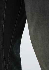 Jeans oscuros con un panel lateral gris en contraste, con costuras visibles y un acabado texturizado. La tela parece suave y duradera.