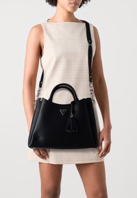 Černá kožená kabelka s pevnou strukturou, texturovaným povrchem, dvojitými rukojetmi a odnímatelným ramenním popruhem. Obsahuje stříbrné kovové doplňky a logo.