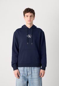 Felpa in cotone blu navy con tasca frontale, corde regolabili e logo sul petto. Caratterizzata da polsini e orlo a coste.