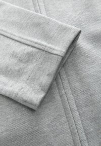 Tessuto di cotone grigio con una texture liscia, che mostra un bordo della manica piegato e dettagli di cucitura visibili.