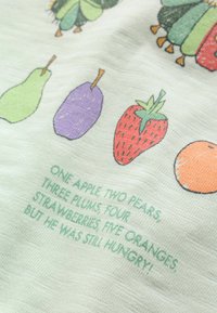Dessins d'une poire, d'une prune, d'une fraise et d'une orange avec un texte listant les fruits et une ligne évoquant le fait d'avoir encore faim sur un tissu.