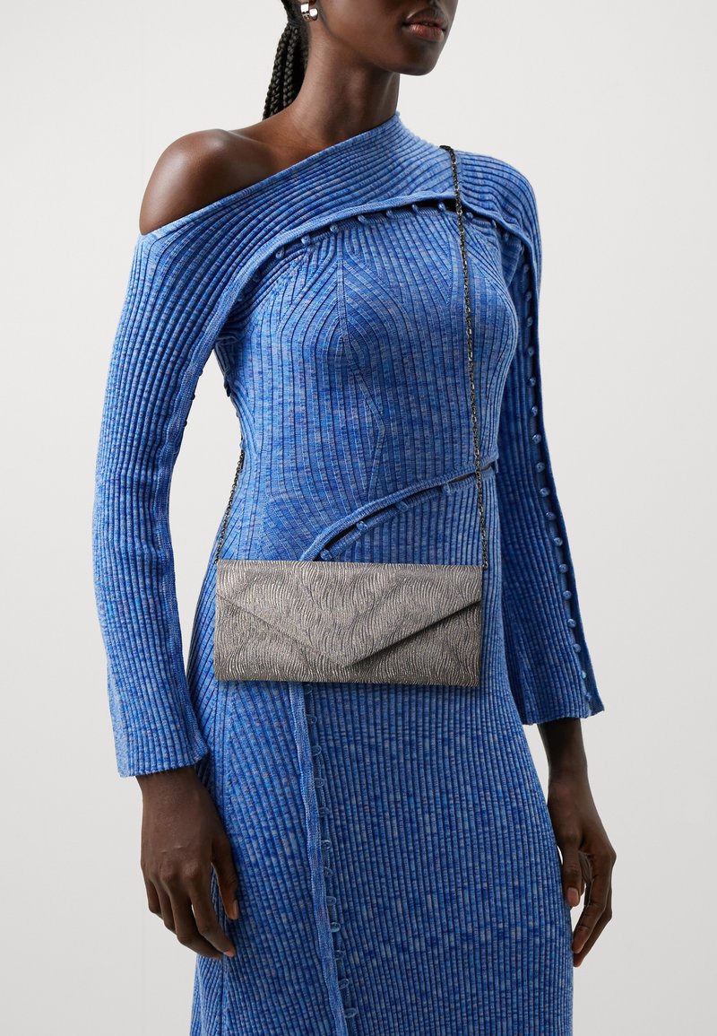 Vestido azul acanalado con diseño off-shoulder y mangas largas. Clutch sobre con textura y patrón ondulado en color gris, llevado cruzado.