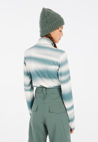 Langarm, getailleerd top met een blauw-wit gestreept patroon; gecombineerd met hooggesneden, groene broek. Breipatroon, textuur groene beanie.